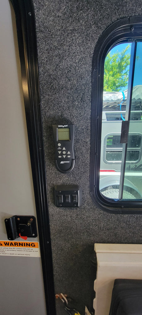 RV rental interior: MaxxAir fan remote, control switches, and a window for exterior views. Essential RV controls.