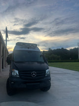 Sleek black Mercedes Sprinter van, ideal for RV rental adventures, parked under a beautiful sunset sky.
