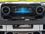 Detailed shot of a Mercedes-Benz Sprinter RV rental dashboard. Its infotainment screen displays phone, settings, and apps, with climate controls.