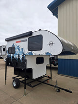 Compact truck camper on a specialized trailer, featuring mountain graphics and an awning, perfect for rv rental trips.