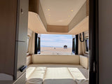 Cozy RV rental interior with light wood and cream cushions, offering a stunning beach and ocean view from the open back doors.