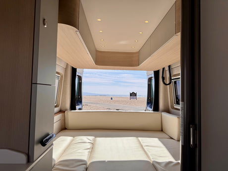 Cozy RV rental interior with light wood and cream cushions, offering a stunning beach and ocean view from the open back doors.