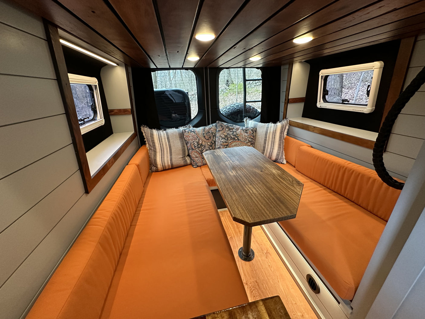Stylish RV rental interior with comfortable orange banquette seating, wooden table, and forest views.
