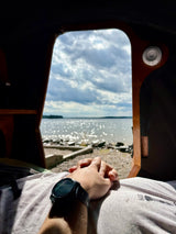 Cozy RV rental interior looking out at a sparkling lake and cloudy sky. Person's hands clasped with smartwatch.