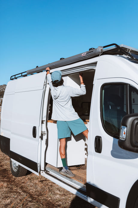 Stepping into adventure! A person adjusts the awning on their white RV rental van, ready for the open road and van life.