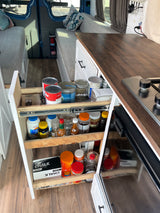 Inside an RV rental: a well-organized pull-out kitchen pantry filled with essentials and a compact stovetop setup.