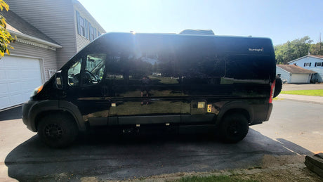 Profile view of a sleek black Sunlight camper van, parked on a driveway for an RV rental.