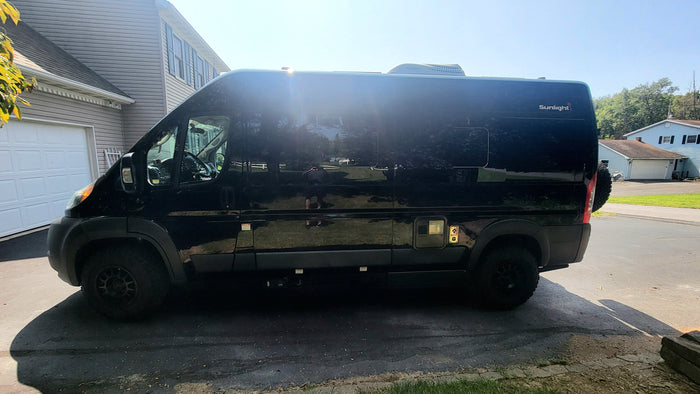 Profile view of a sleek black Sunlight camper van, parked on a driveway for an RV rental.