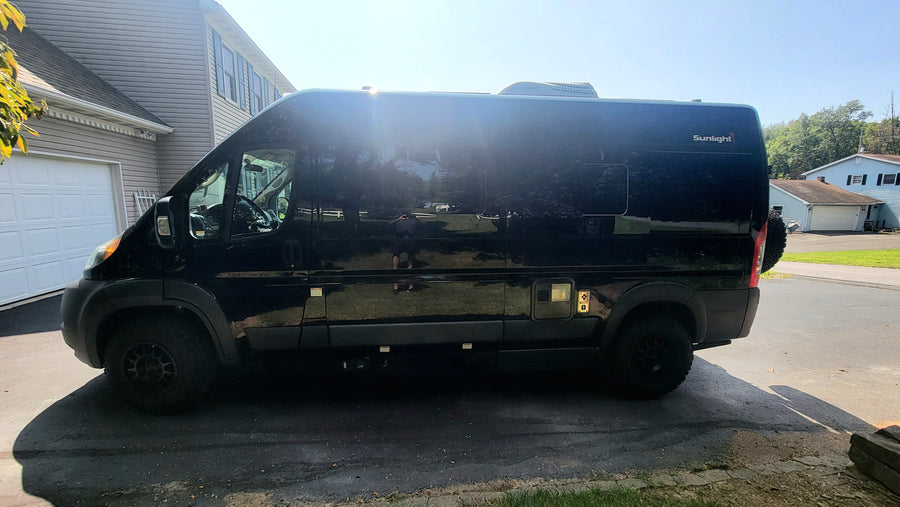 Profile view of a sleek black Sunlight camper van, parked on a driveway for an RV rental.