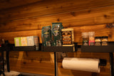 Organized shelves in an RV rental kitchen hold Trader Joe's coffee, teas, and spices. A paper towel roll is mounted below.