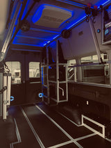 Inside a sleek RV rental van, showcasing custom blue LED lighting, a JL Audio system, modular aluminum shelving, and floor tracks.