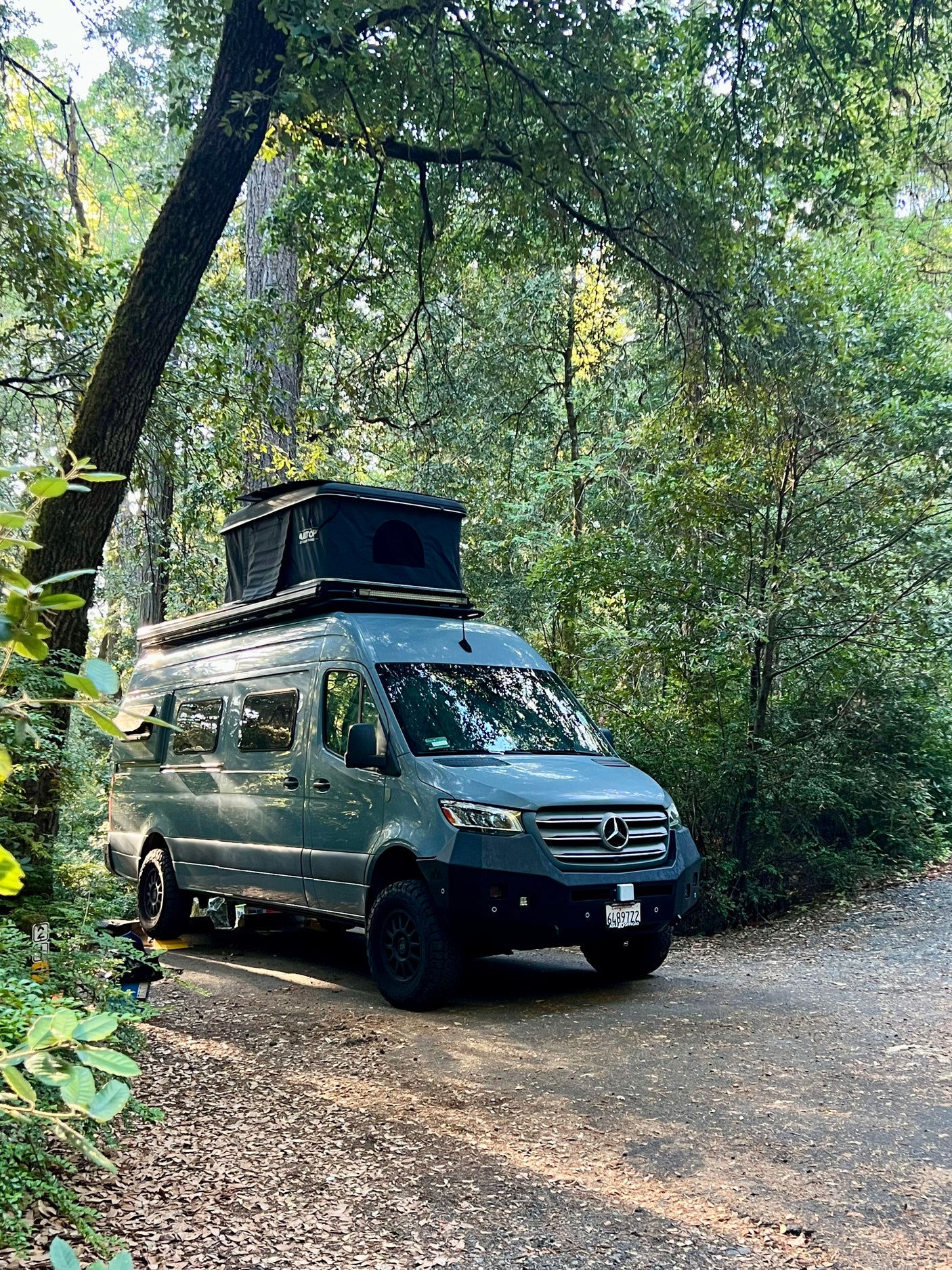 Adventure-ready gray Mercedes Sprinter camper van for rv rental, parked in a lush forest campsite. Ideal for outdoor travel.