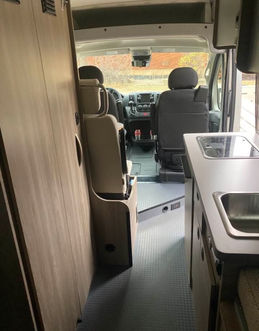  stands next to a red RV rental camper van by a river in a forest.|This RV rental features a well-equipped campervan interior with kitchen — photo 6