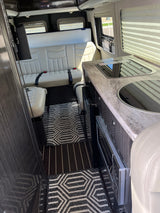 Spacious RV rental interior with light leather seating, a modern kitchen counter, and integrated appliances, ideal for travel.