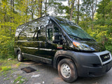 Black Ram ProMaster 2500 RV rental parked in a lush forest, featuring a 'hello' mat. Perfect for outdoor travel.