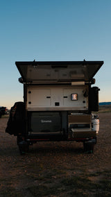 Rear view of an open overland camper trailer's outdoor kitchen, with a Truma fridge and pull-out stove. Consider this for your rv rental.