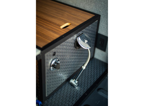 RV rental: Compact utility module with pull-out shower head, wood top, and patterned surfaces inside a camper van.