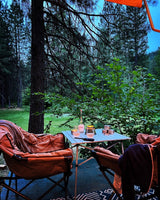 RV rental: Peaceful camping setup with two chairs and a table holding rosé and glasses, surrounded by lush forest.