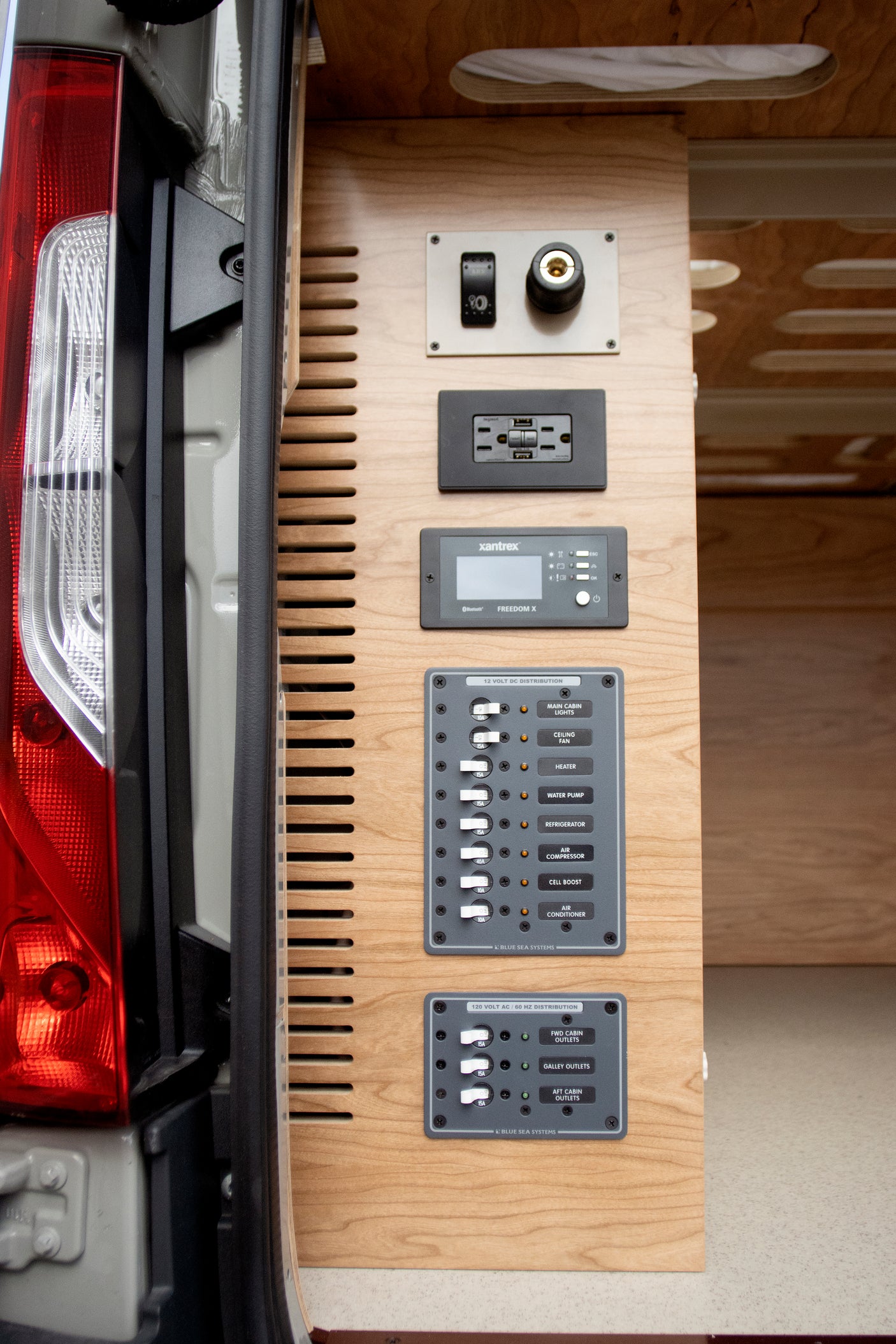 Inside an RV rental: detailed view of a camper van's sophisticated electrical control and power distribution system on wood paneling.