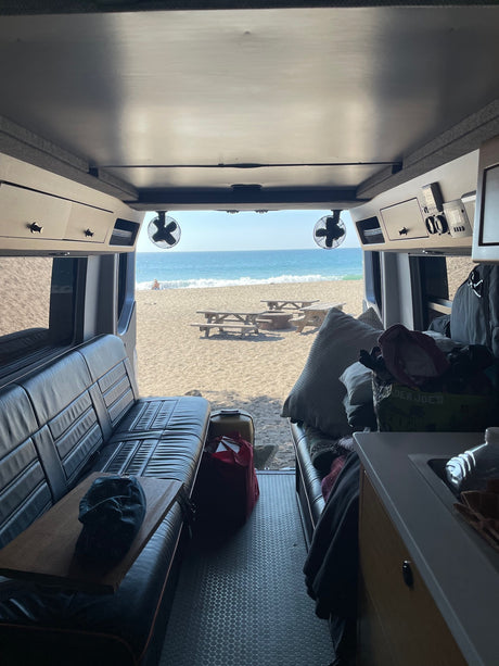 Cozy RV rental interior facing out to a sandy beach with the ocean, waves, and picnic tables. Ultimate beach camping!