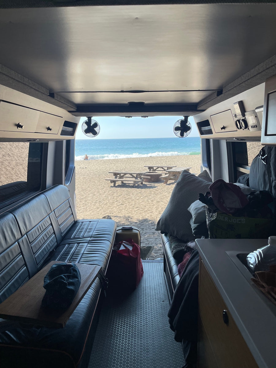 Cozy RV rental interior facing out to a sandy beach with the ocean, waves, and picnic tables. Ultimate beach camping!