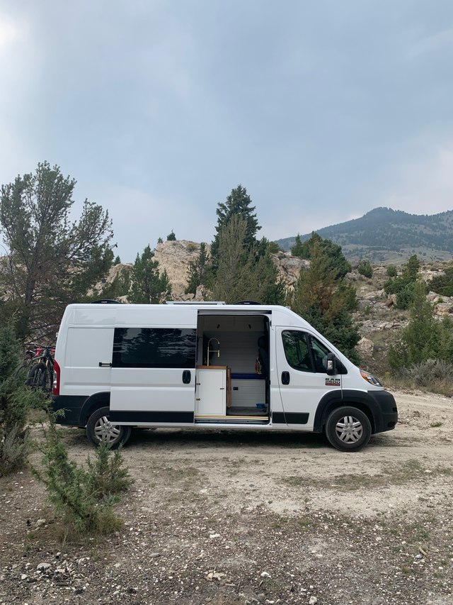 White camper van (RV rental) with open side door revealing interior, parked in a rocky mountain landscape. Perfect for van life.