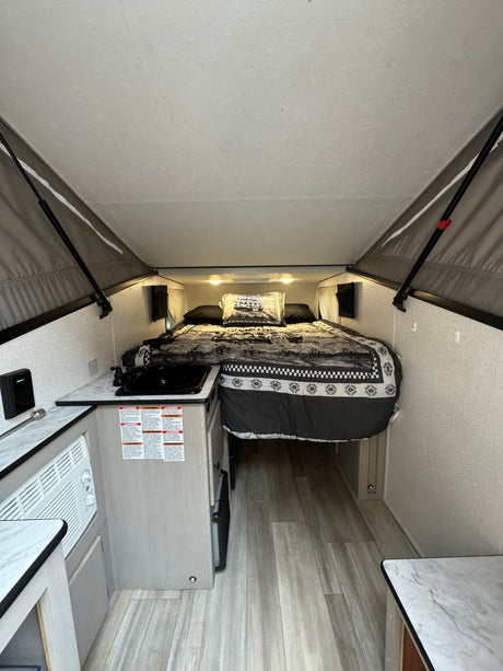 Inside a compact RV rental: a comfortable bed with themed bedding, small kitchen, and AC unit. Ready for camping trips.