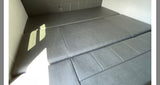 Inside an RV rental, grey upholstered cushions are arranged as a comfortable convertible bed. Sunlight brightens the modern space.