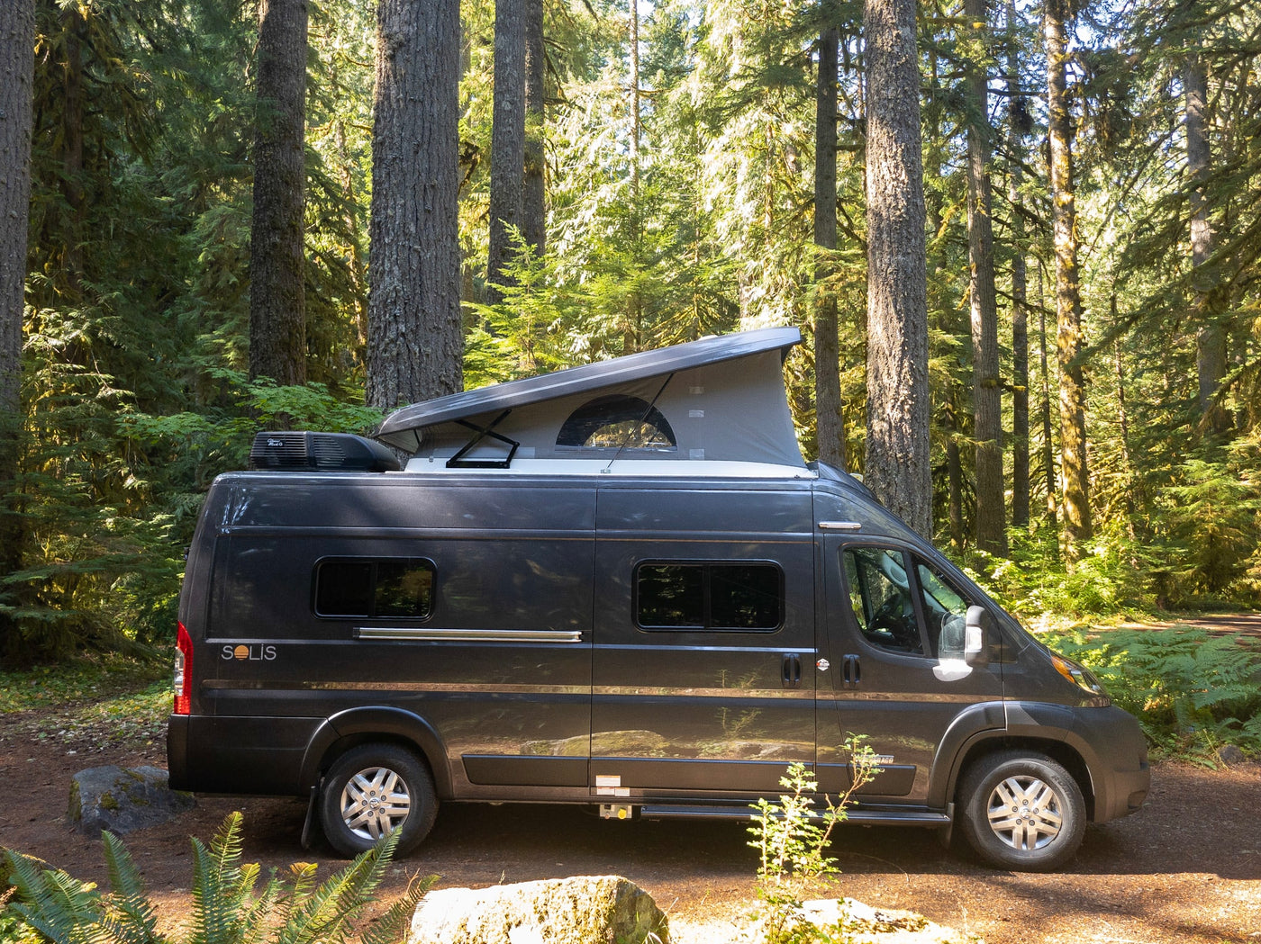  a girl colors at a dinette table. A kitchen counter & bed are also visible.|Dark gray Solis camper van with pop-top extended — photo 8