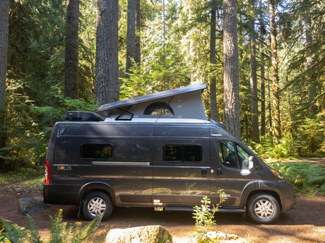 Dark gray Solis camper van with pop-top extended, parked in a sun-dappled forest. Book your rv rental for nature escapes!