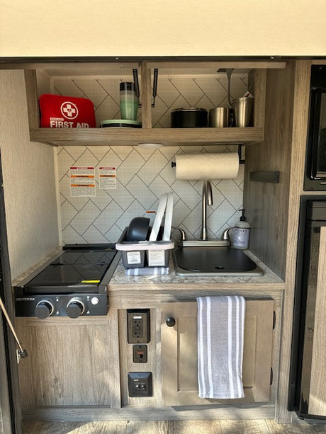 Inside an RV rental: compact kitchen featuring a sink, stove, microwave, and neatly organized cooking essentials.