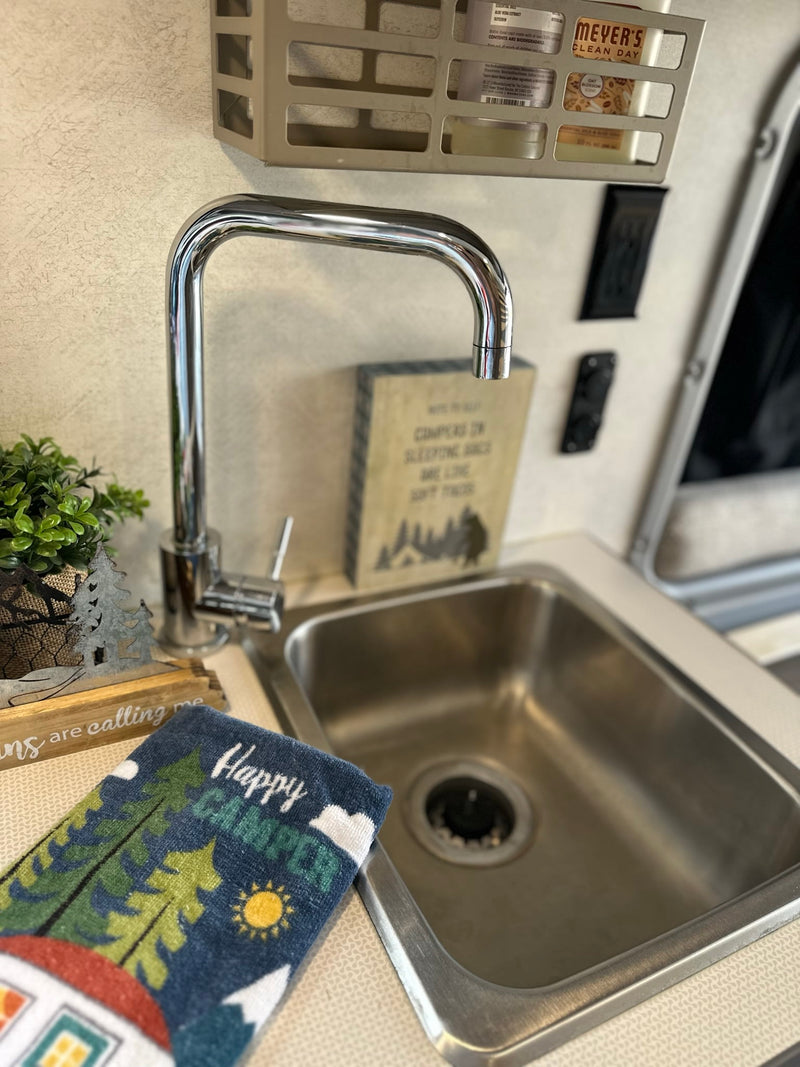 Functional RV rental kitchen sink with chrome faucet, "Happy Camper" towel, plant, and Meyer's soap. — photo 8