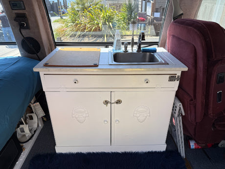 Experience your RV rental's compact kitchen: sink, cutting board, and cozy interior comforts for your journey.