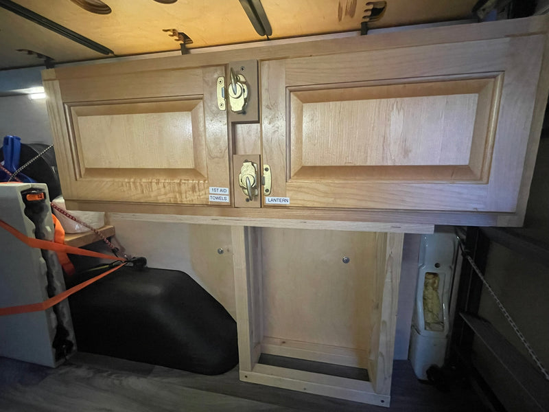 Customized wooden overhead cabinets and floor storage maximize space in this RV rental interior, with labeled compartments for easy access. — photo 13