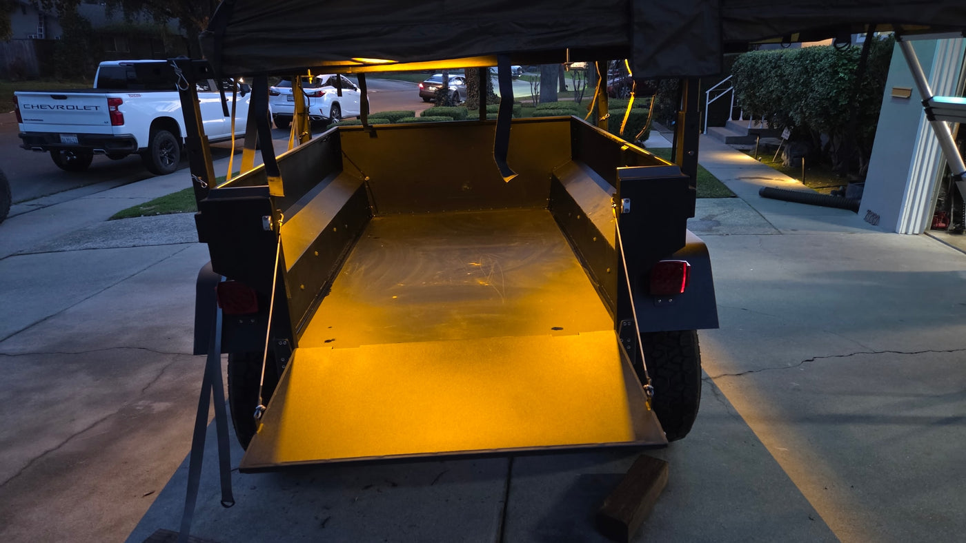 Illuminated overland trailer with tailgate down, parked near a white Chevy truck. An ideal RV rental for your next outdoor adventure. — photo 5