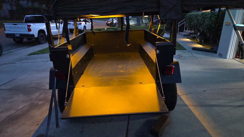 Illuminated overland trailer with tailgate down, parked near a white Chevy truck. An ideal RV rental for your next outdoor adventure. — photo 5