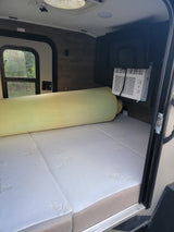 RV rental interior: A mattress with a rolled foam topper, a window AC unit, and an EXIT sign above the side window.