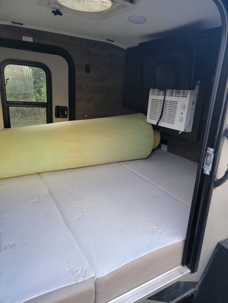 RV rental interior: A mattress with a rolled foam topper, a window AC unit, and an EXIT sign above the side window.