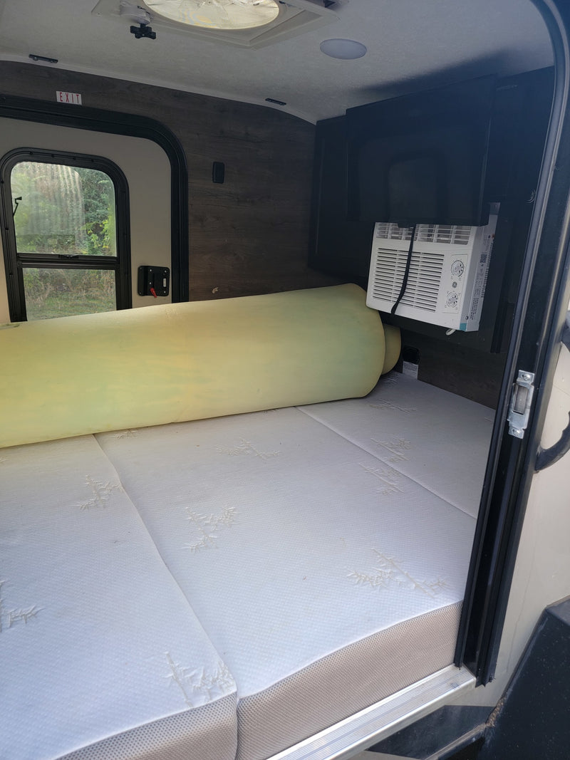 RV rental interior: A mattress with a rolled foam topper, a window AC unit, and an EXIT sign above the side window. — photo 4