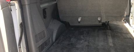 RV rental interior: Rear cargo area with a dark carpeted floor, a bench seat with buckles, and side wall paneling.