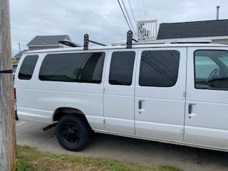 A white commercial van, with tinted windows and a roof rack, possibly for an RV rental conversion.