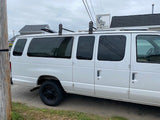 A white commercial van, with tinted windows and a roof rack, possibly for an RV rental conversion.