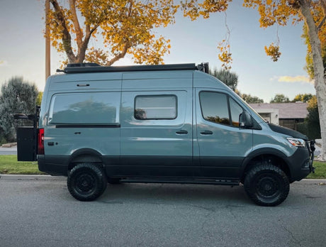 Explore with this gray Mercedes Sprinter camper van, modified with off-road tires & roof rack, ideal for an RV rental adventure.