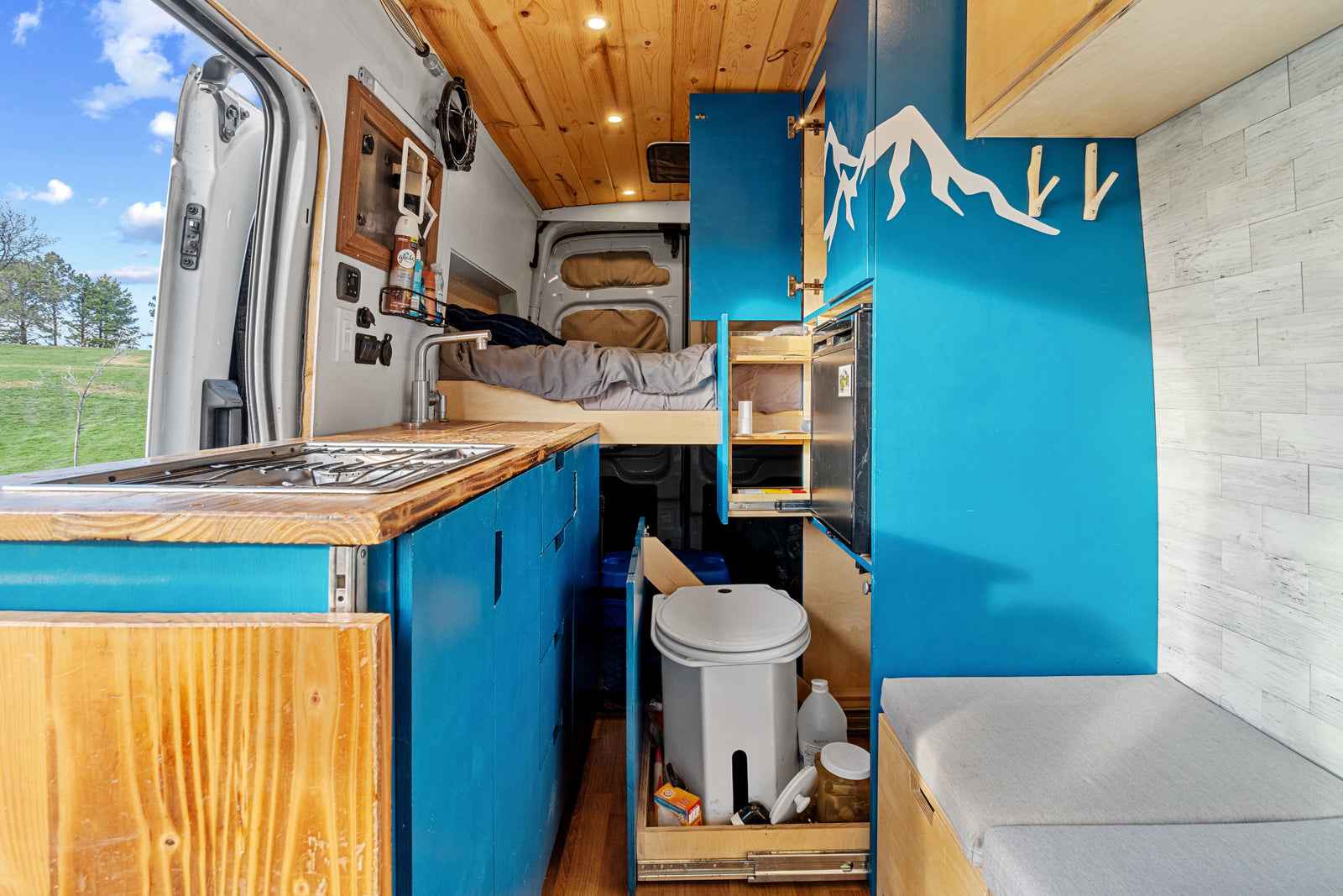 rv rental: custom camper van interior featuring kitchenette, bed, storage, and a discreet pull-out toilet for travel.