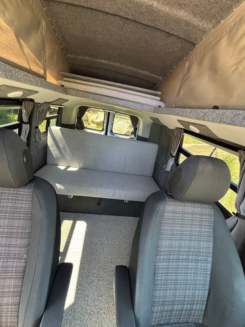 Spacious RV rental interior featuring a grey convertible bench seat/bed and an extended pop-top roof with lights. — photo 11