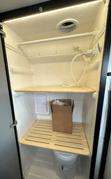Inside an RV rental's compact wet bath, showcasing a toilet, shower, and adaptable slatted shelves for space optimization.
