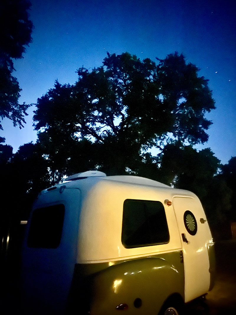 A small, retro rv rental parked at night under dark trees and a starry blue sky, ready for adventure. — photo 4