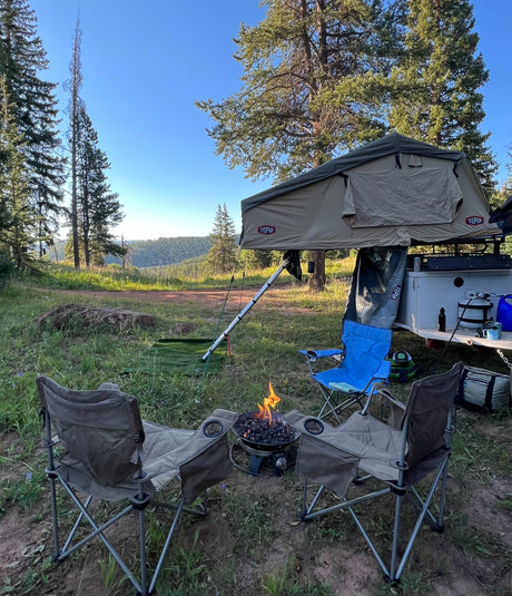 Peaceful **rv rental** camping with a rooftop tent, chairs, and a cozy campfire amidst a scenic forest.
