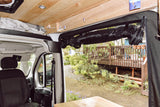 RV rental interior with wooden ceiling, rolled black screen, and garden view from the open side door.