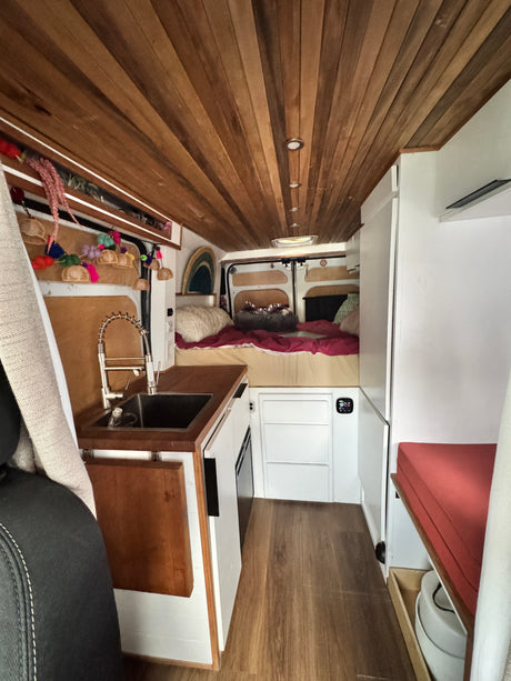 Spacious camper van interior, ideal for an rv rental, featuring a kitchenette, rear bed, and cozy wooden ceiling.